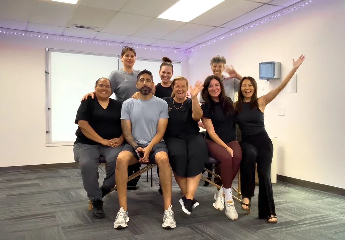 Yodi Richeson smiling and waving with a group of practitioners in her training room.
